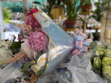 Punch H wrapped in light blue cellophane with a pink and light blue ribbon, peonies and astilbe peeking out
