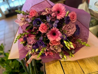 Field of Dreams: pink gerbera daisies and roses, purple anemones and green snapdragons in lavender wrap, lying on a table