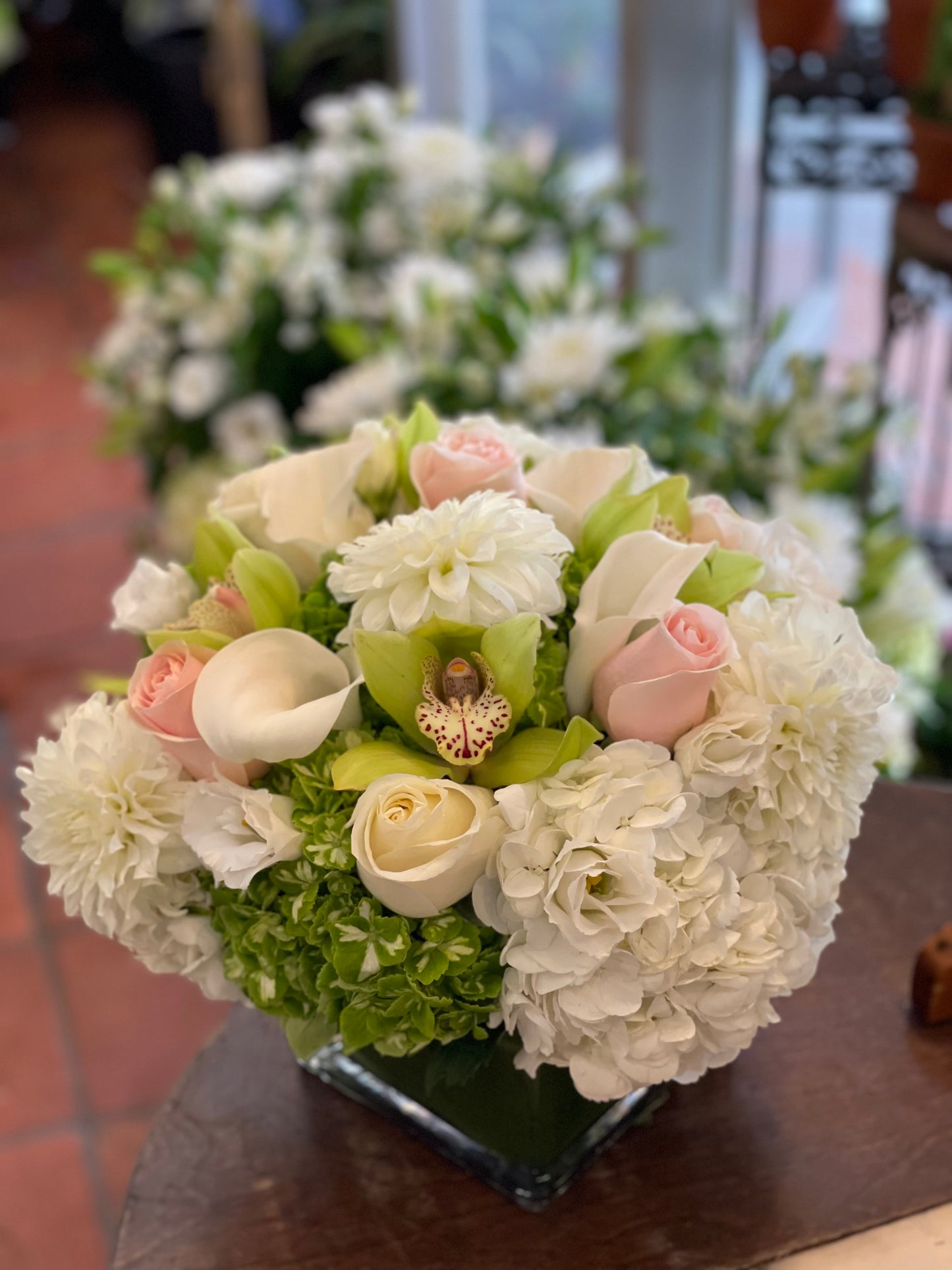 Kakovatos white and green hydrangea, white callas and dahlias, blush roses and green cymbidium orchids in a glass cube