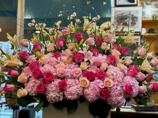 Knockout full view, white blossom branches and cream lilies rising above pink hydrangea and hot pink roses in a white box