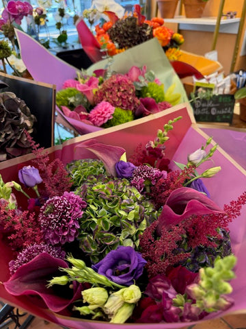 Green Envy, medium size: purple lisianthus, burgundy callas and astilbe over green hydrangea, other bouquets behind