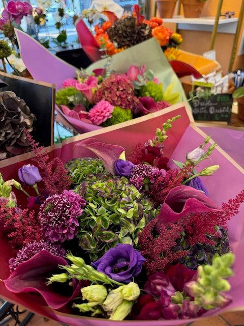 Green Envy, medium size: purple lisianthus, burgundy callas and astilbe over green hydrangea, other bouquets behind