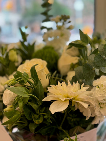 Erly Afternoon side view: white dahlia and cream roses with eucalyptus and green foliage by the shop window