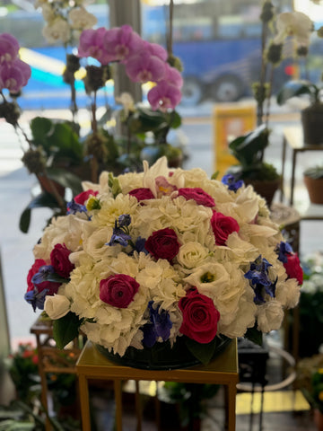 White Fire small size, low round bowl of white hydrangea with hot pink roses, crimson ranunculus and blue delphinium