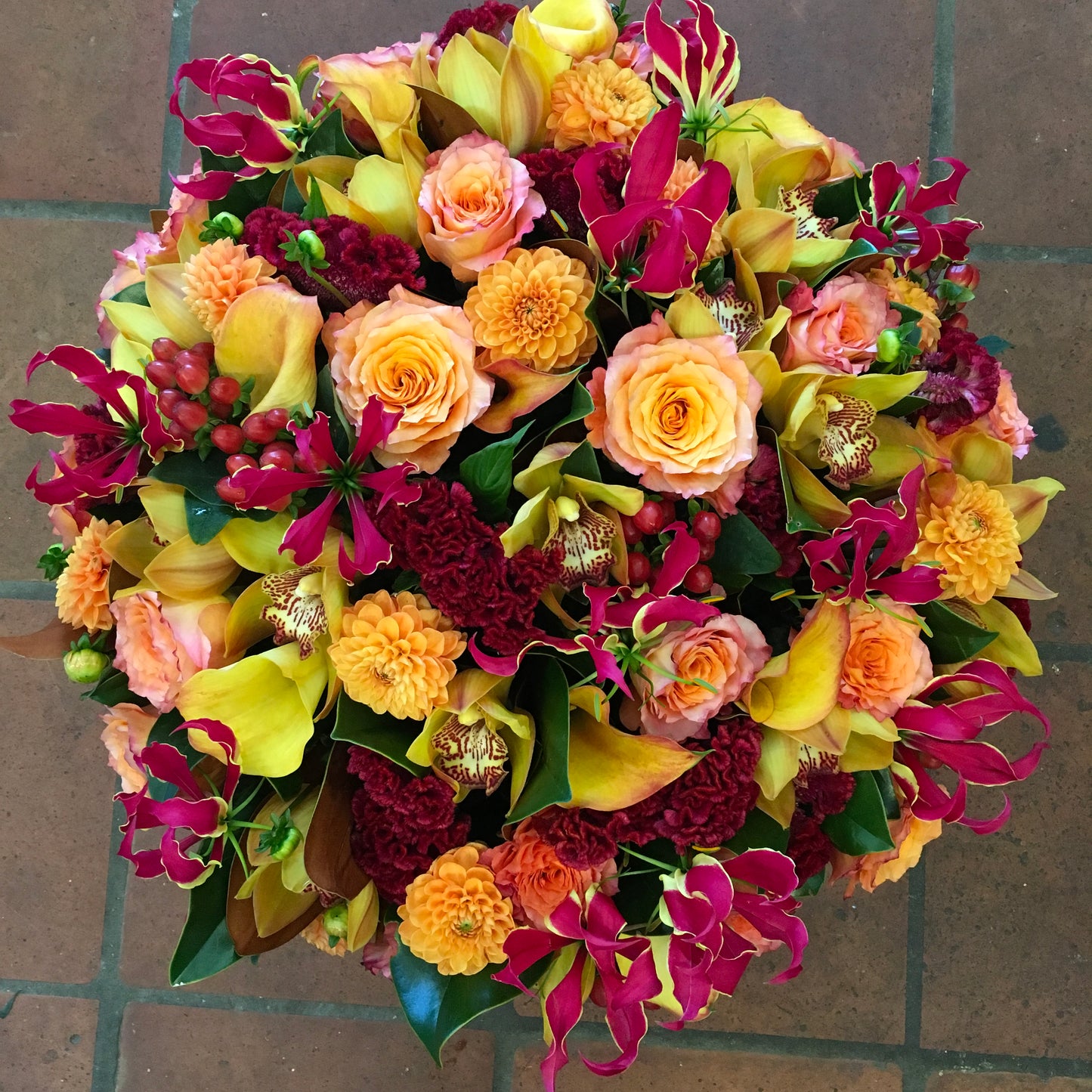 Red Berry seen from above: orange roses and dahlias, gloriosa lilies, yellow callas, cymbidium orchids and red berries