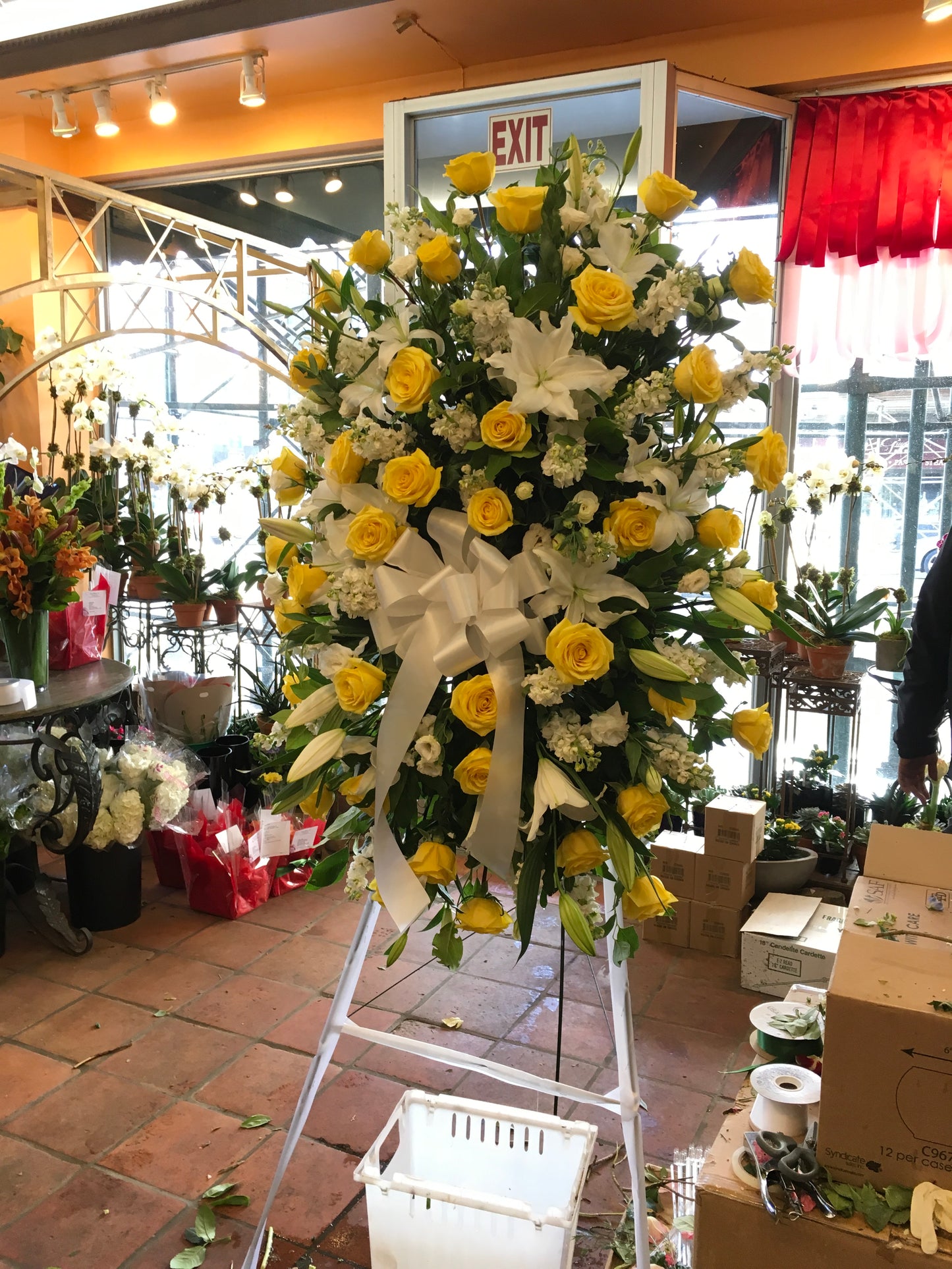 Tranquility medium and large size, yellow roses and white lilies with a white bow on a standing easel