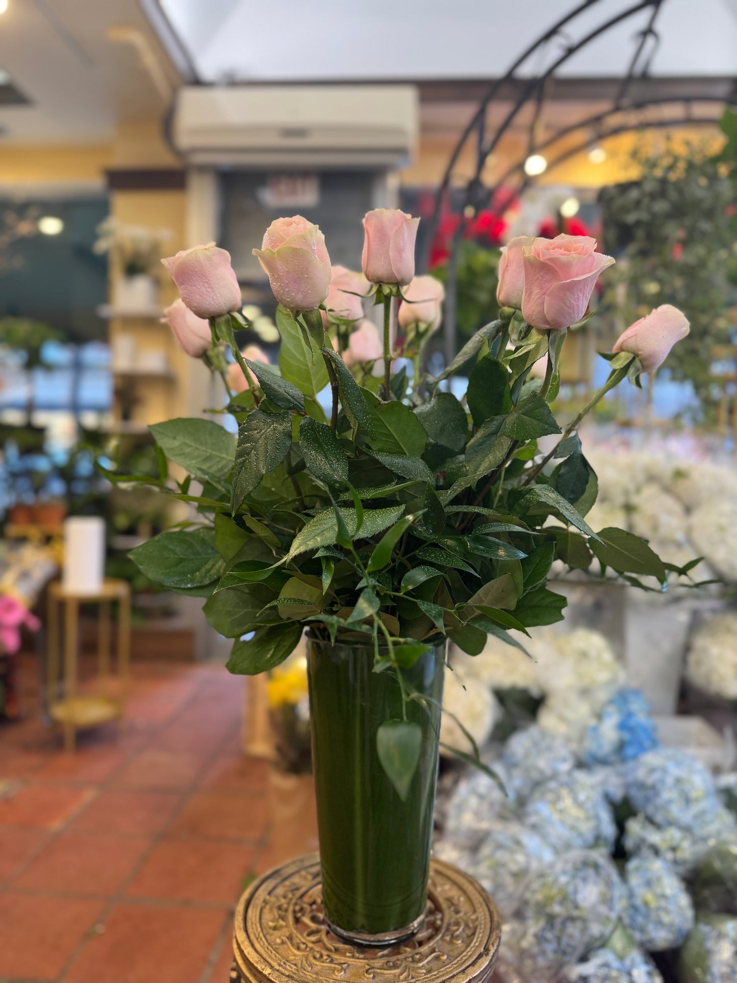 Pink Roses, light pink long-stem roses with greenery in a tall leaf-lined glass vase in the shop