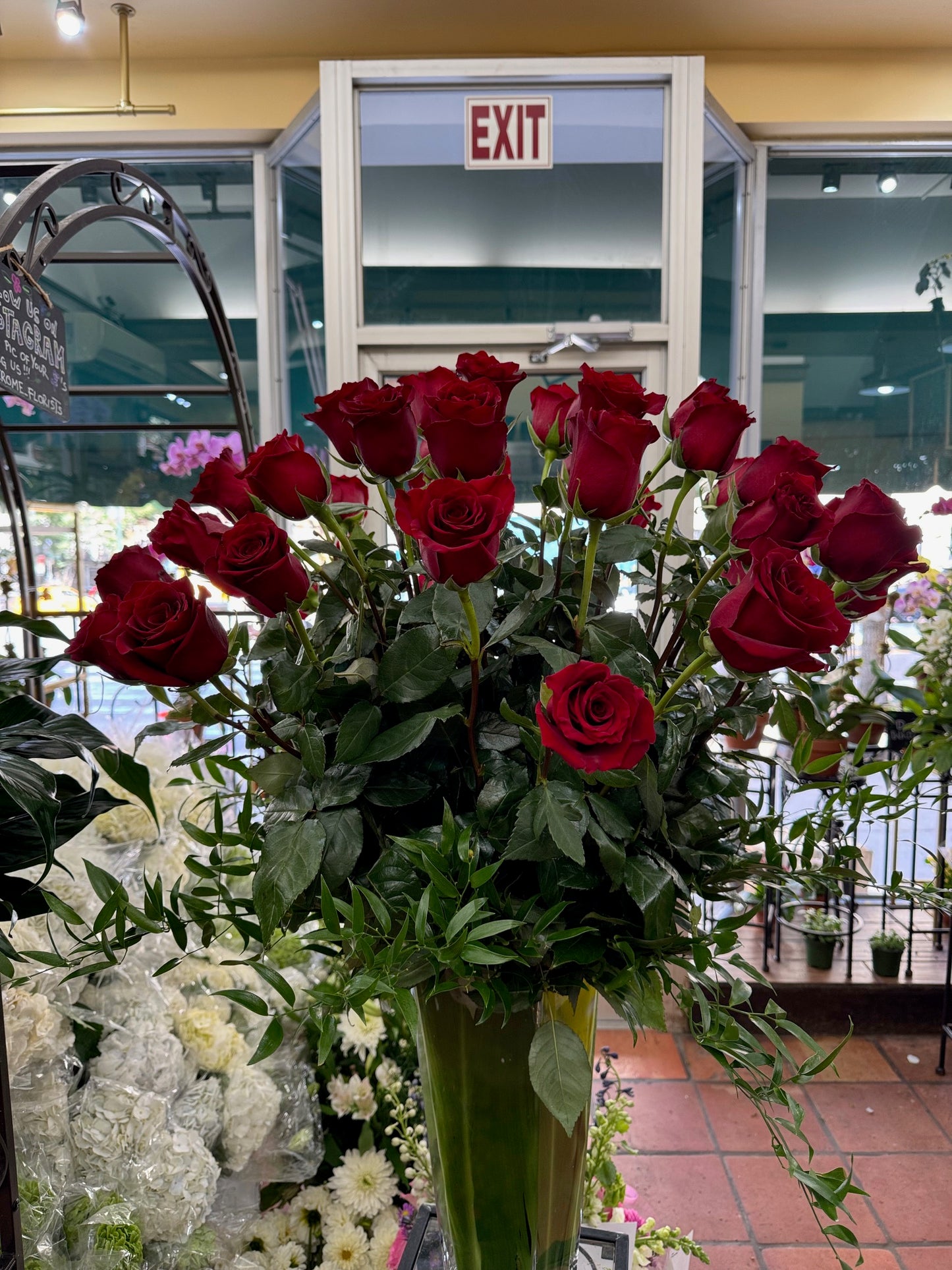 Red Explorer Roses, medium size, tall red roses with trailing greenery in a leaf-lined vase in the shop
