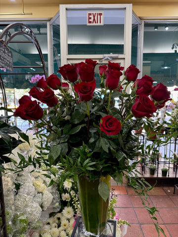Red Explorer Roses, tall red roses and trailing greenery in a leaf-lined vase, front view
