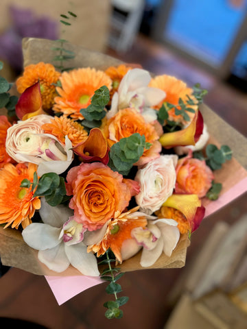 Erly Riser from above: orange gerbera daisies, peach-orange roses and white cymbidium orchids with eucalyptus in kraft wrap
