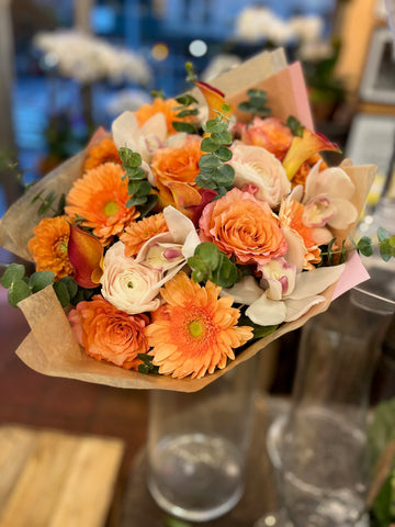 Erly Riser, large with vase: orange roses, gerberas and white cymbidium orchids in kraft paper set in a clear glass vase
