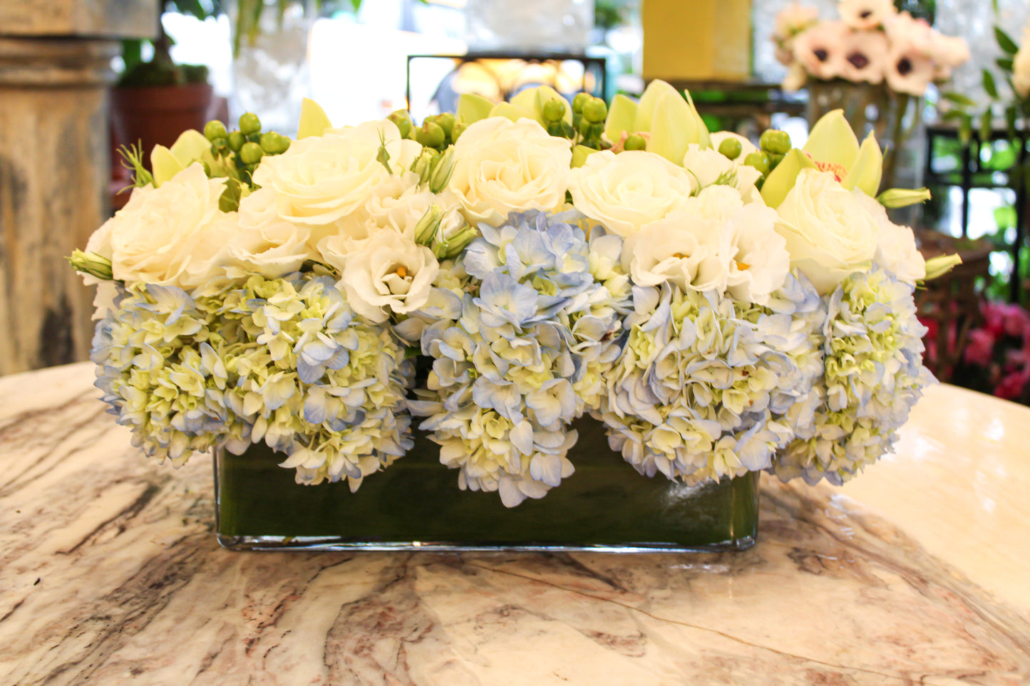 Blue Dream small size, Square vase option: white roses and green orchids over pale blue hydrangea in low leaf-lined glass