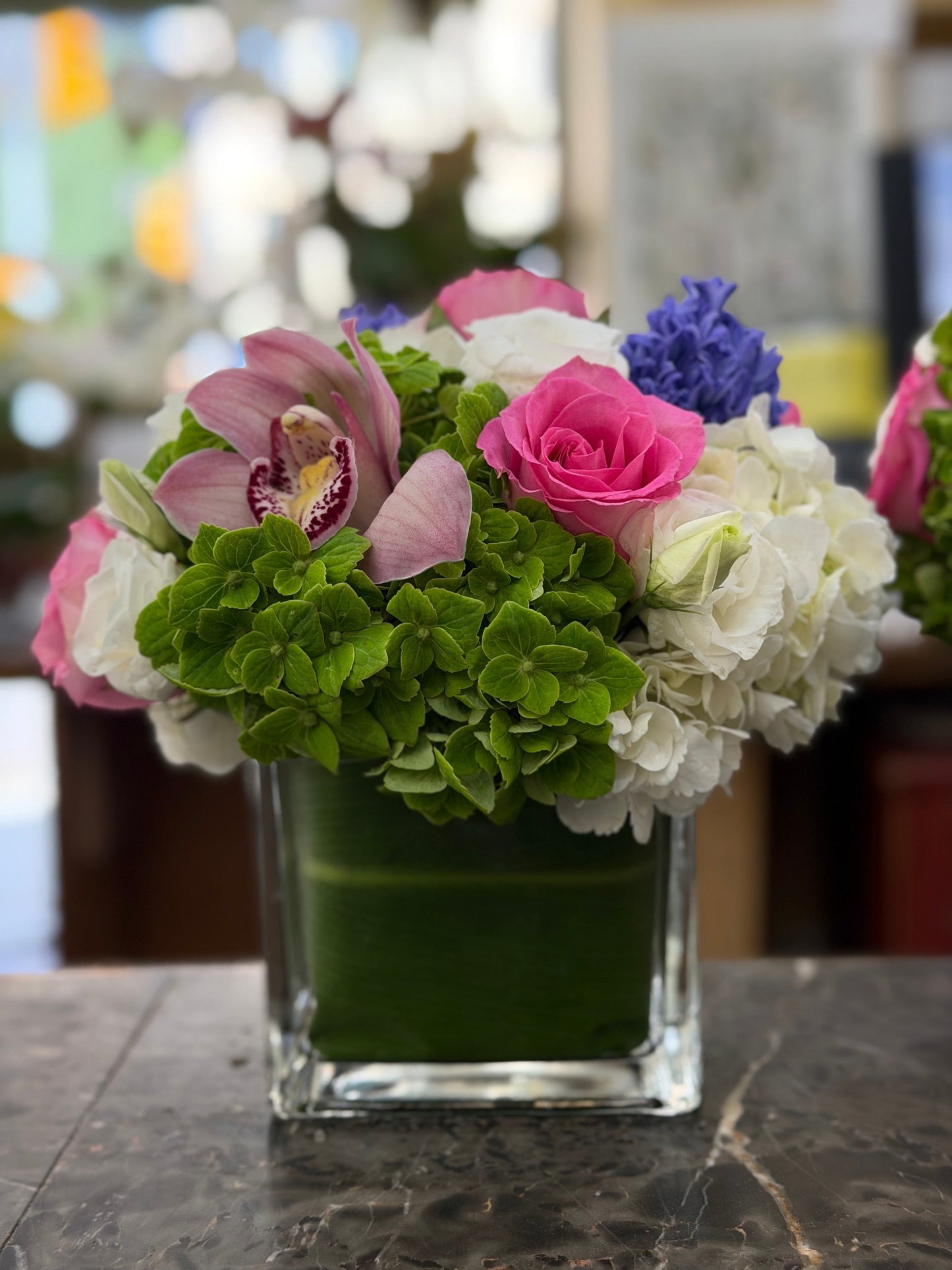 Close view of Eliana on dark veined marble: green hydrangea in front, hot pink rose, speckled pale pink cymbidium orchid