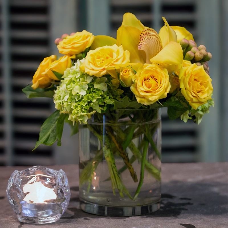 Simply Yellow, yellow roses, a yellow cymbidium orchid and green hydrangea in a clear glass cylinder vase