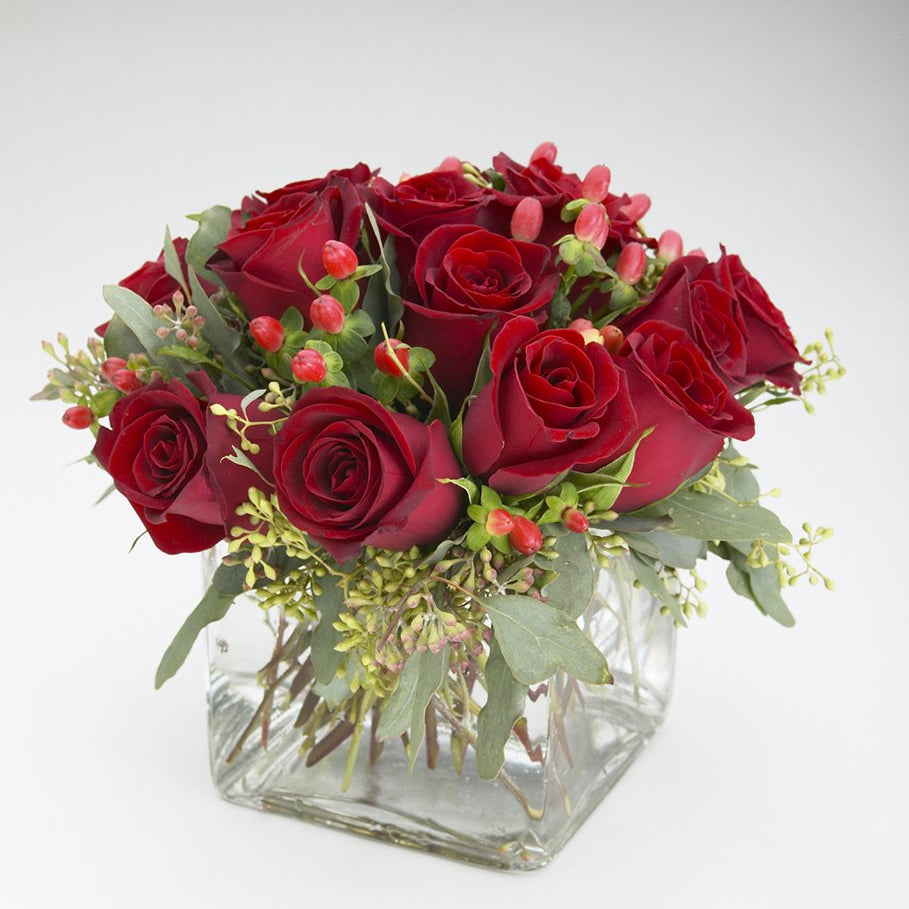 Scarlet Rose, deep red roses with red hypericum berries and seeded eucalyptus in a clear glass cube vase