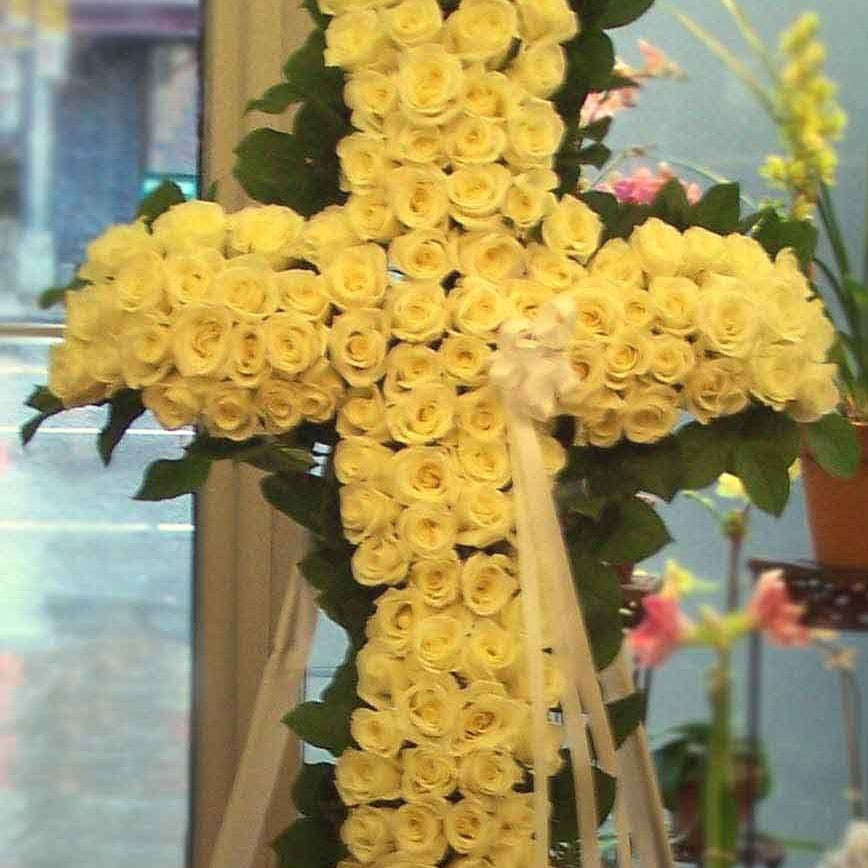 Divine - Sympathy Cross of pale yellow roses and greenery on a standing easel with cream ribbon