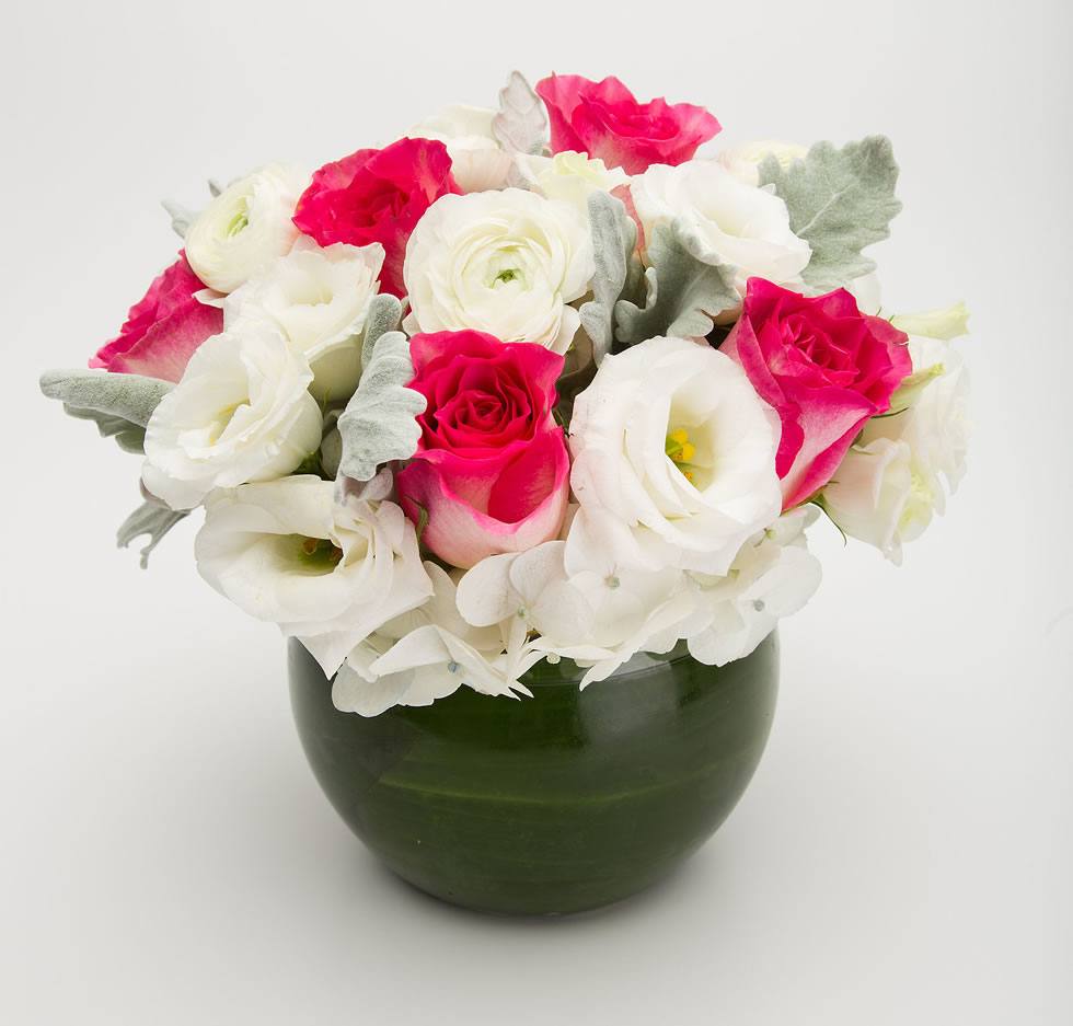 Rose Bowl with hot pink roses, white ranunculus, lisianthus and dusty miller in a leaf-lined round glass bowl