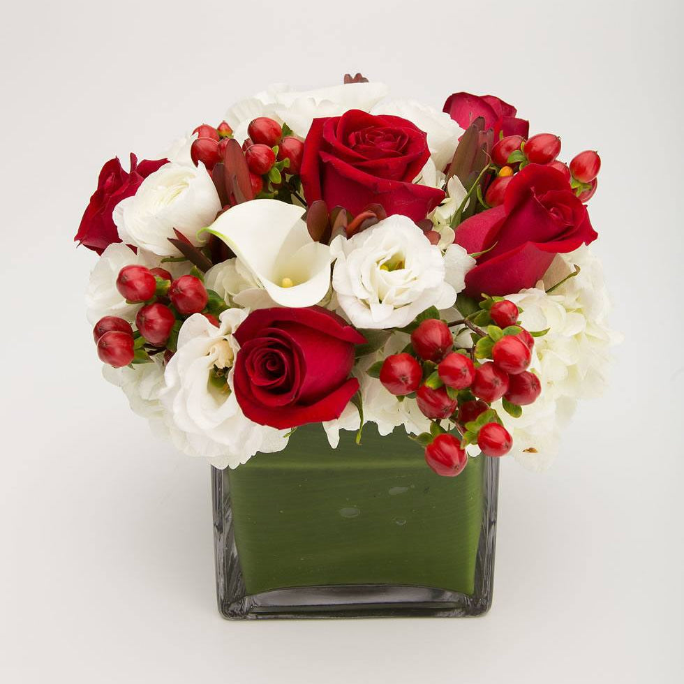 Crimson arrangement of red roses, red hypericum berries, white hydrangea, lisianthus and a calla lily in a leaf-lined cube