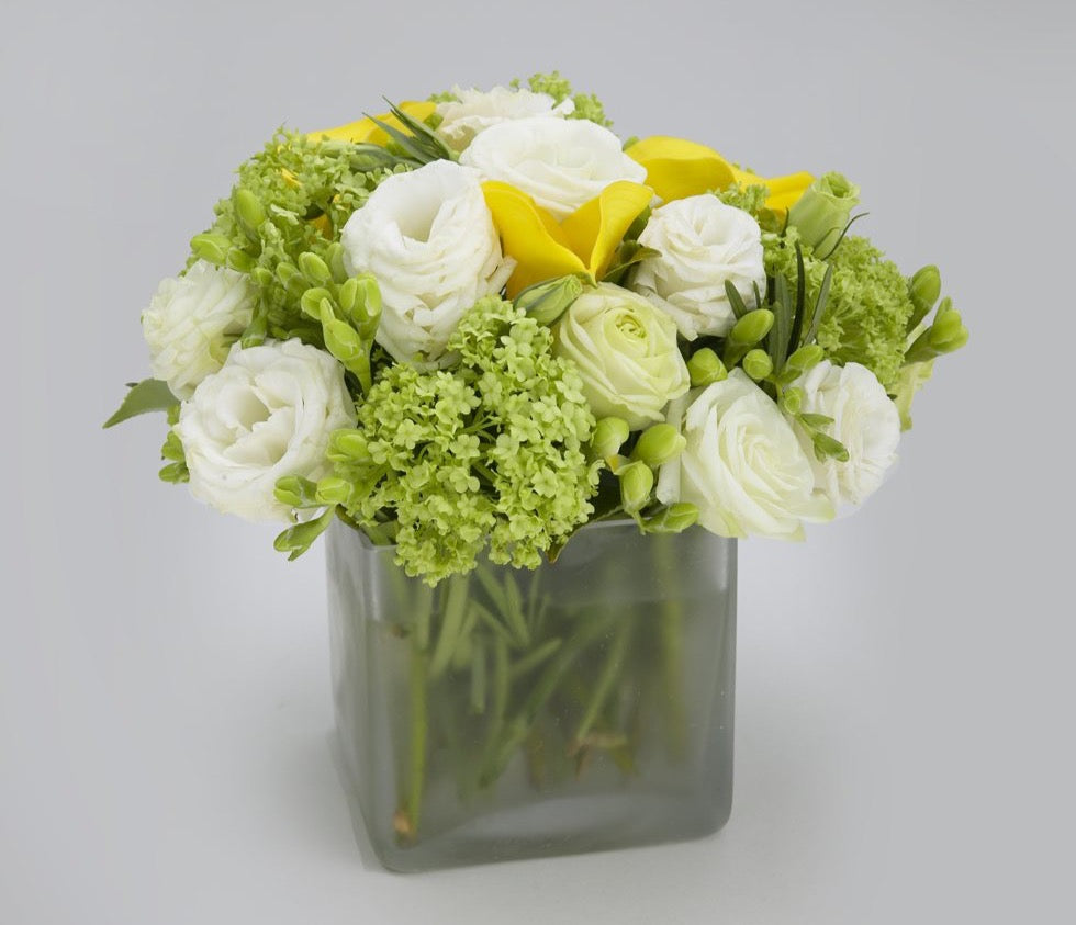 Sweet Nothing, white lisianthus and roses, yellow calla lilies and green viburnum in a frosted glass cube vase