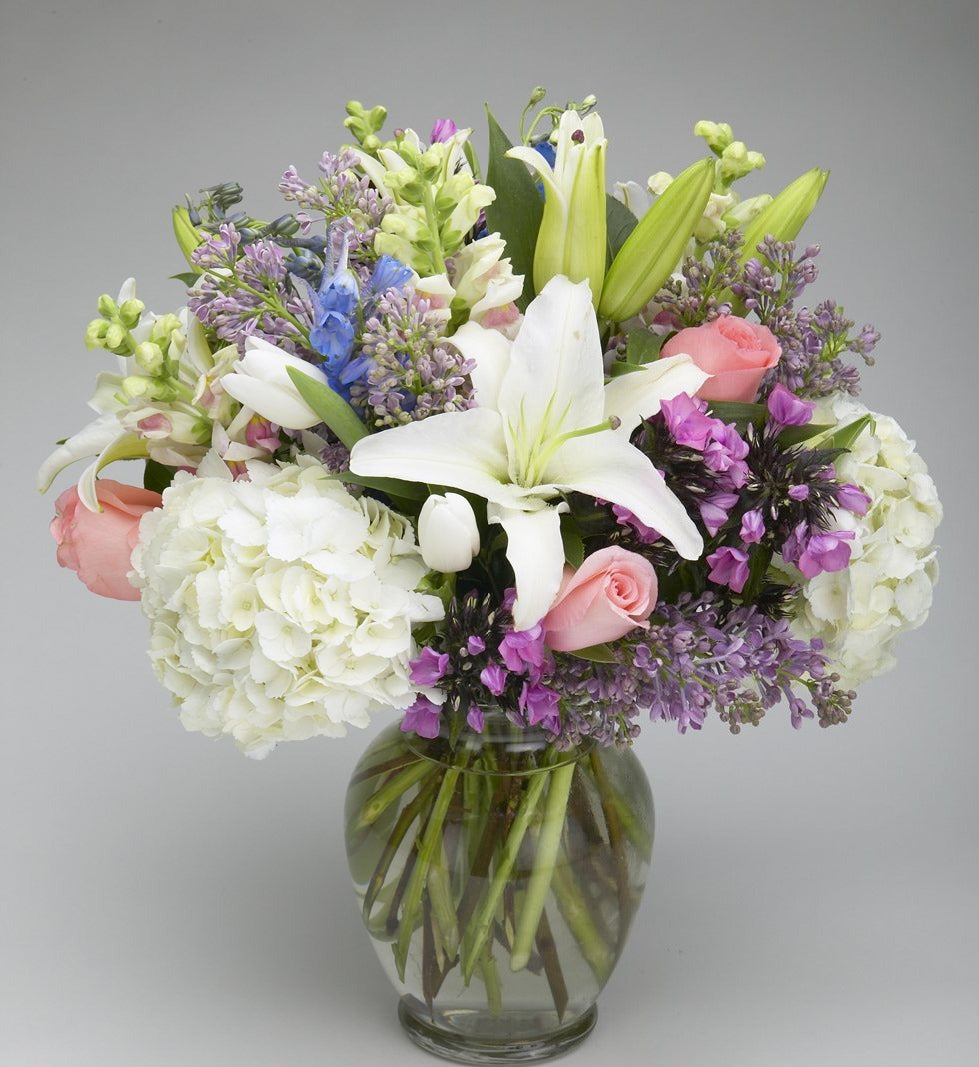 White lilies, hydrangea, pink roses and lilac in a clear glass vase