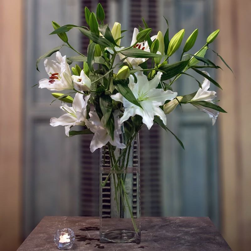 Tall white lilies arranged in a clear rectangular glass vase