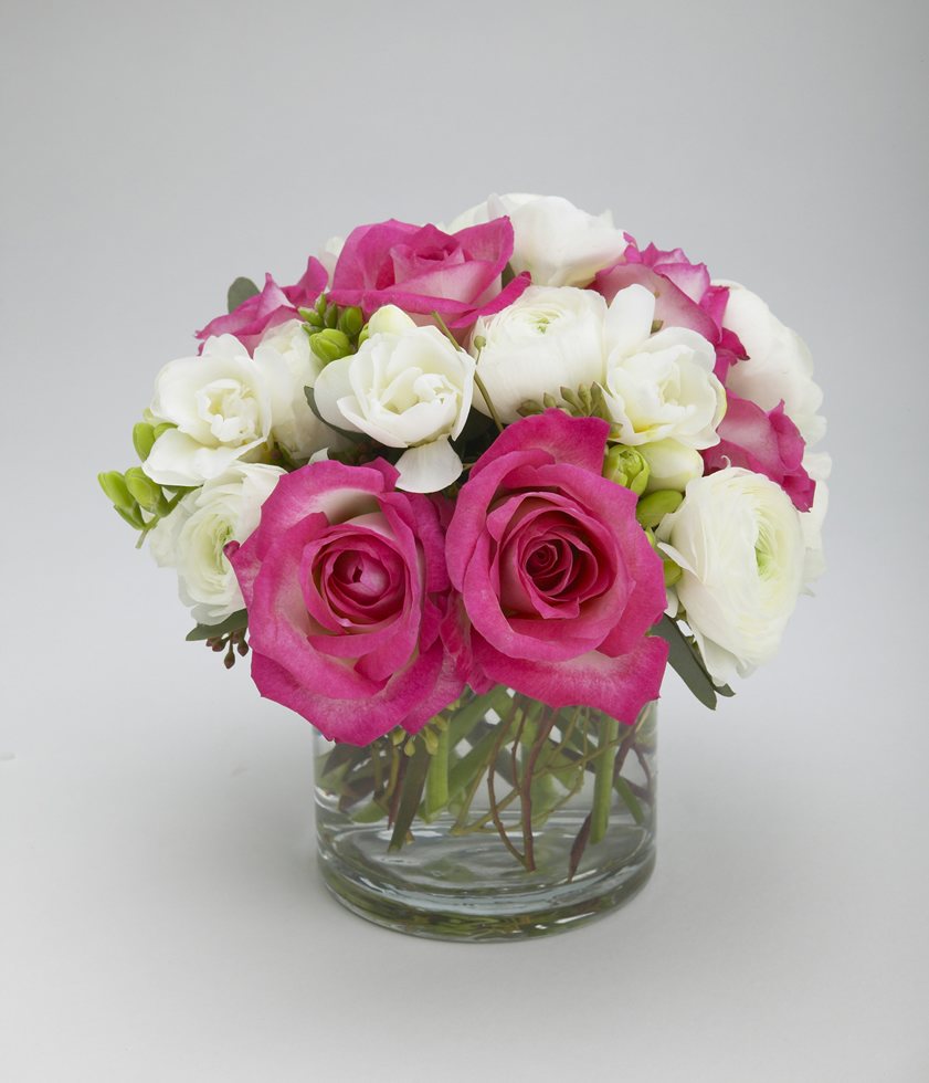 Hot pink roses with white ranunculus and freesia in a glass cylinder