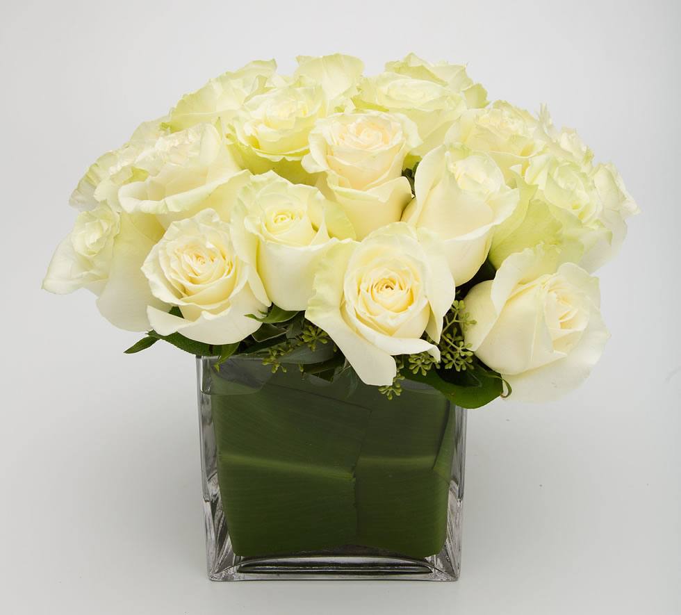 Cream-white Mondial roses gathered in a leaf-lined glass cube