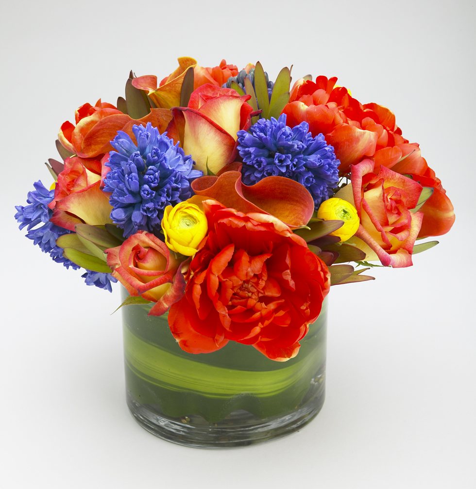 Orange tulips, roses and callas with blue hyacinth in a leaf-lined vase
