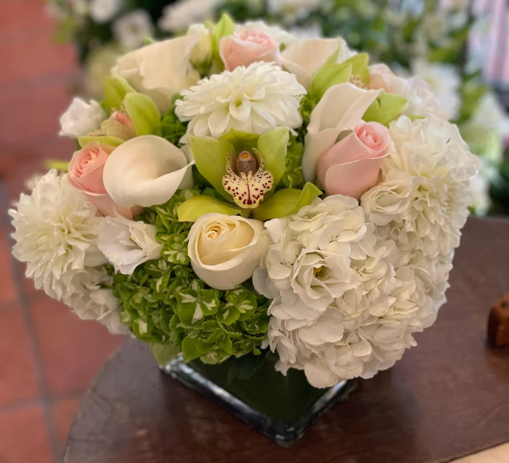 Glass cube of white dahlias, white hydrangea, callas, blush roses and a green cymbidium orchid