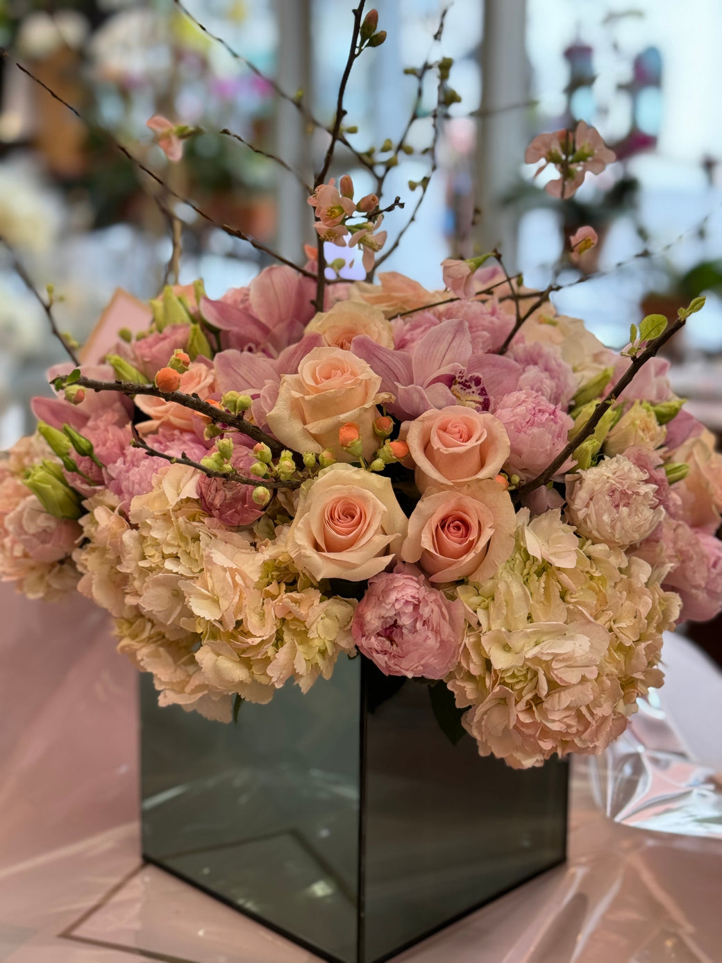 Peach roses, pink peonies, orchids, hydrangea and blossom branches in a vase