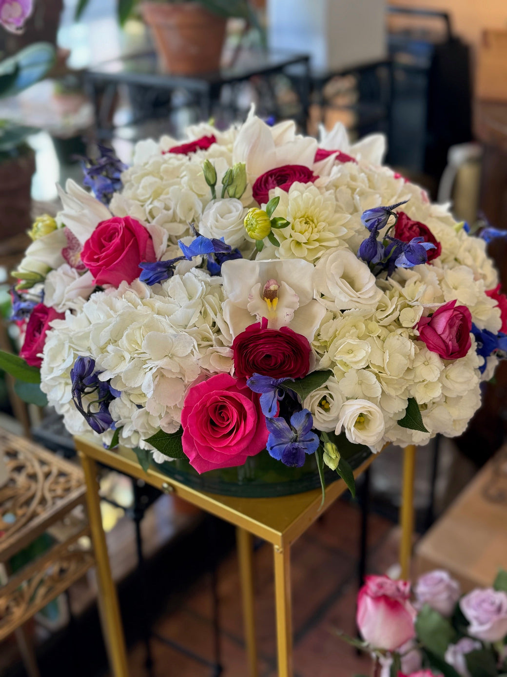 Low white hydrangea dome with hot pink roses, red ranunculus, white orchids and blue delphinium