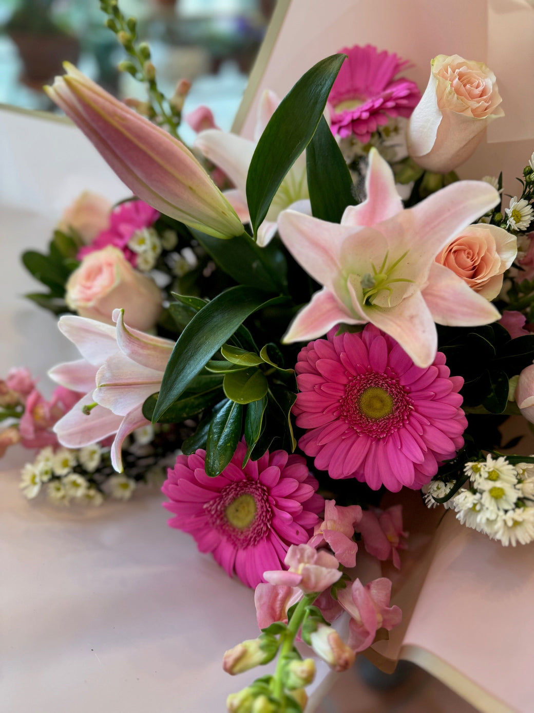Wrapped bouquet of pink lilies, hot pink gerberas, peach roses and snapdragons