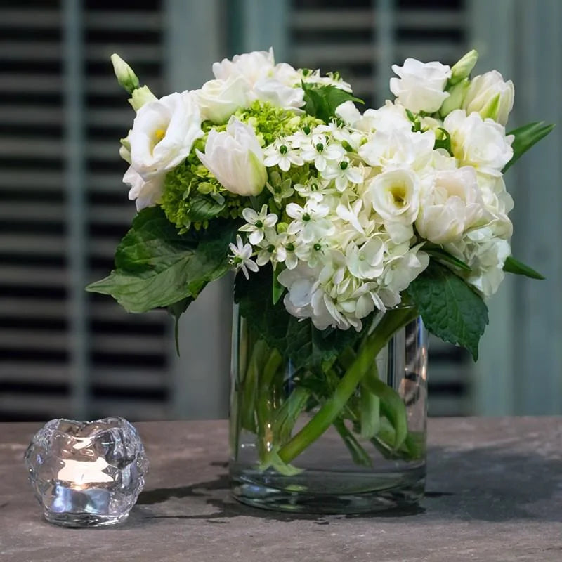 White lisianthus with green hydrangea and small white star-shaped flowers in a clear glass vase