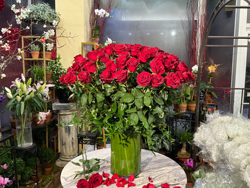 
                    
                      Complete Love small size: one tall glass vase of long-stem red roses on a marble table with scattered petals
                    
                  