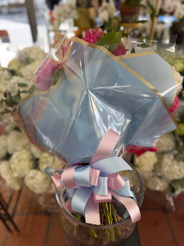 
                    
                      Punch H in light blue cellophane tied with a pink and light blue bow, stems resting in a glass display vase
                    
                  