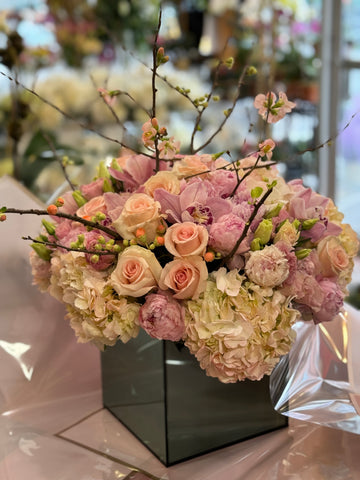 
                    
                      Pink Fury, side view of blush hydrangea, peach roses and pink peonies with blossom branches in a mirrored cube
                    
                  