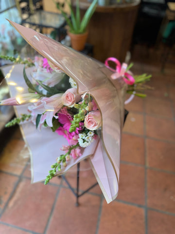 
                    
                      Pink Passion small size: wrapped in clear and blush paper with a pink ribbon, peach roses and snapdragons showing
                    
                  