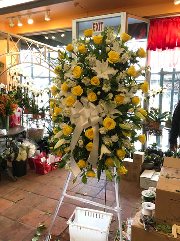 
                    
                      Tranquility medium and large size, yellow roses and white lilies with a white bow on a standing easel
                    
                  