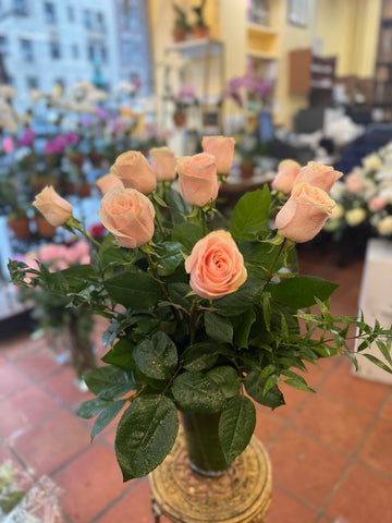 
                    
                      Pink Roses, peach-pink roses with glossy greenery in a tall leaf-lined glass vase on a gold stand
                    
                  
