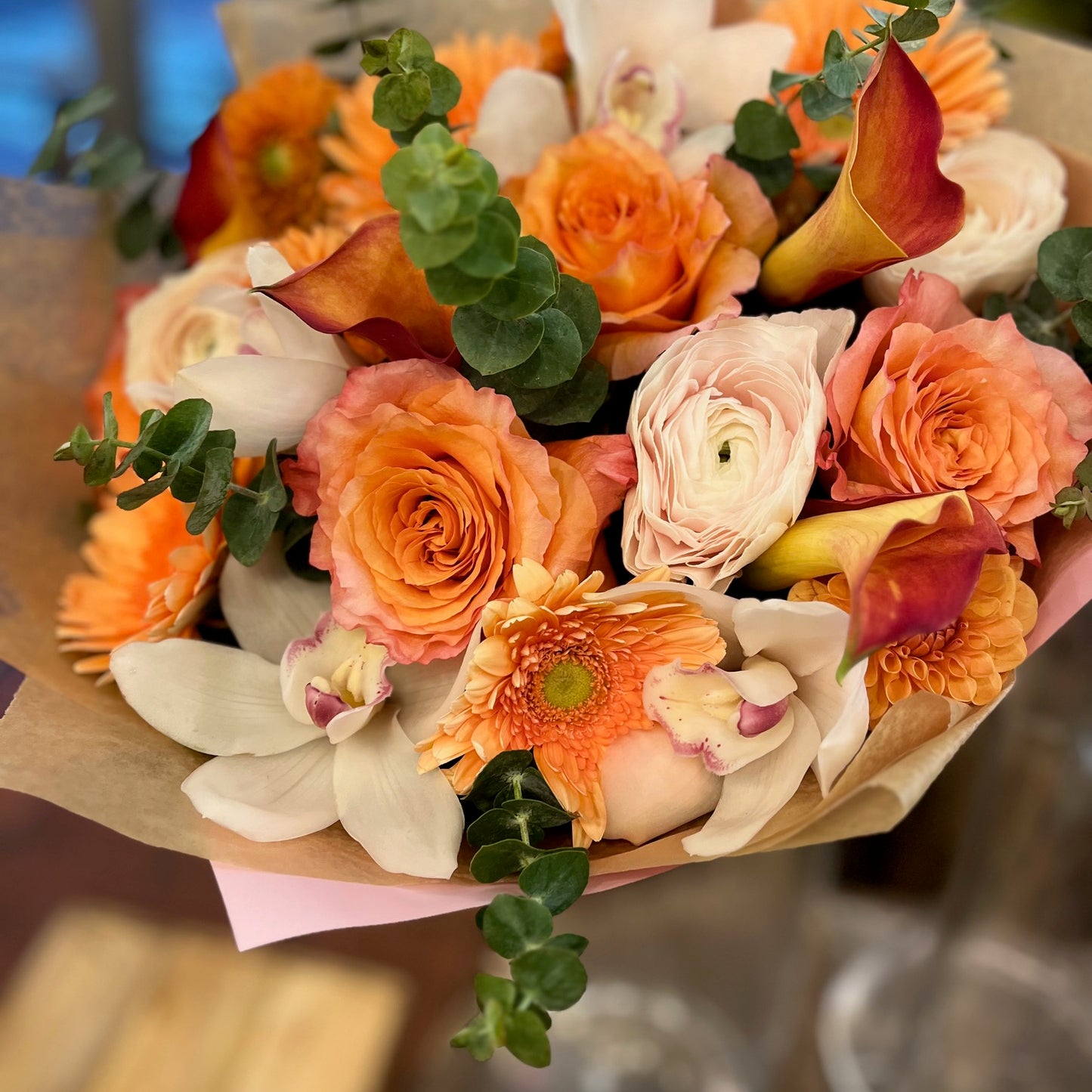 Erly Riser: orange roses, orange gerberas, cream ranunculus, white cymbidium orchids and red-orange callas in kraft paper
