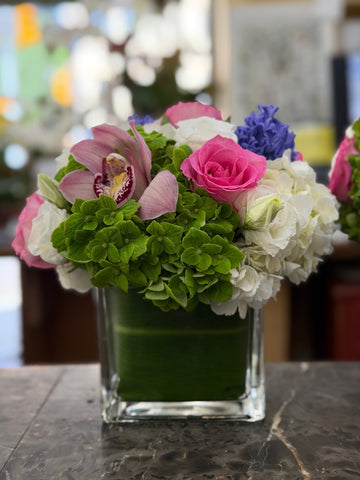 
                    
                      Close view of Eliana on dark veined marble: green hydrangea in front, hot pink rose, speckled pale pink cymbidium orchid
                    
                  
