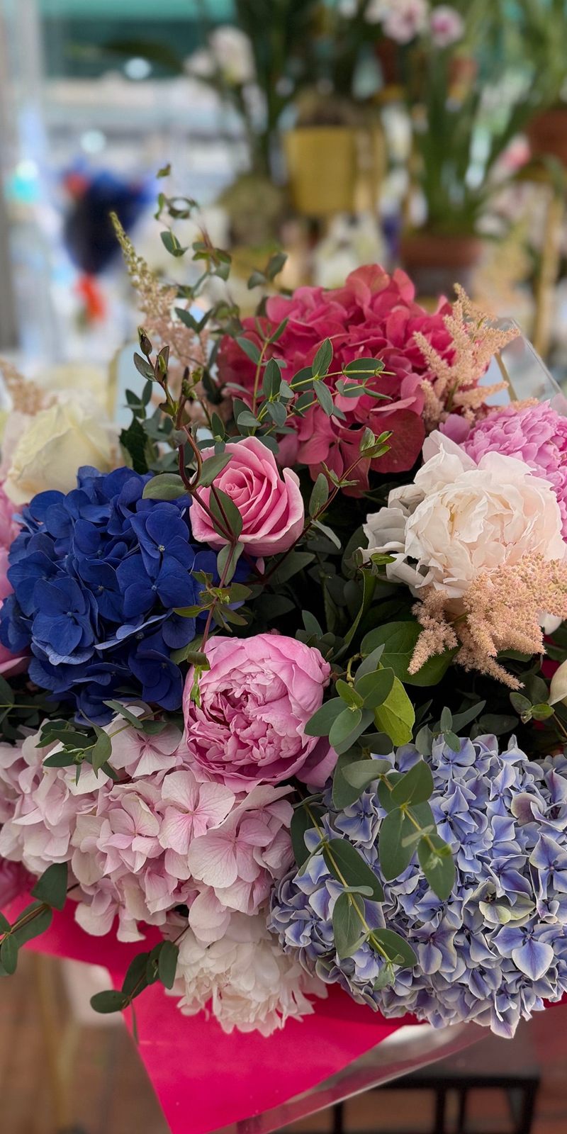 Hand-tied bouquet of blue and pink hydrangeas, pink and white blooms, roses, astilbe and eucalyptus in pink wrapping at Jerome Florists
