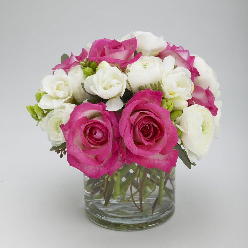 Darling: hot pink roses, white ranunculus and white freesia with green buds in a clear glass cylinder vase